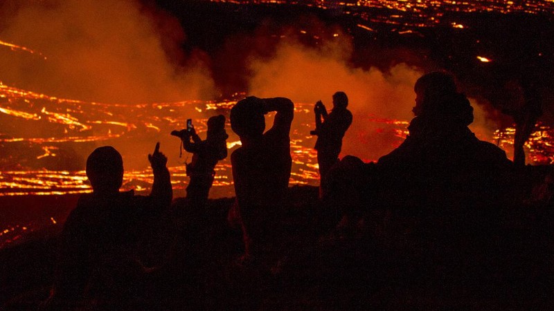 People watch as lava flows from an eruption of a volcano on the Reykjanes Peninsula in southwestern Iceland late on Monday, March 29, 2021. Iceland's latest volcano eruption is still attracting crowds of people hoping to get close to the gentle lava flows. (AP Photo/Marco Di Marco)