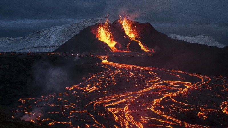 People watch as lava flows from an eruption of a volcano on the Reykjanes Peninsula in southwestern Iceland late on Monday, March 29, 2021. Iceland's latest volcano eruption is still attracting crowds of people hoping to get close to the gentle lava flows. (AP Photo/Marco Di Marco)