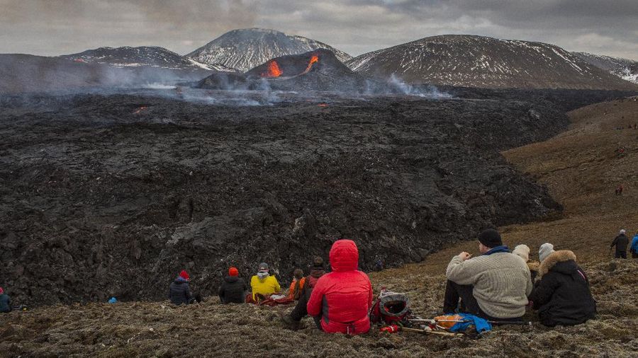 People watch as lava flows from an eruption of a volcano on the Reykjanes Peninsula in southwestern Iceland late on Monday, March 29, 2021. Iceland's latest volcano eruption is still attracting crowds of people hoping to get close to the gentle lava flows. (AP Photo/Marco Di Marco)