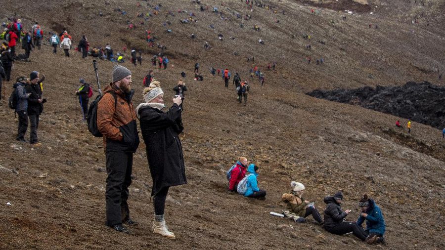 People watch as lava flows from an eruption of a volcano on the Reykjanes Peninsula in southwestern Iceland late on Monday, March 29, 2021. Iceland's latest volcano eruption is still attracting crowds of people hoping to get close to the gentle lava flows. (AP Photo/Marco Di Marco)