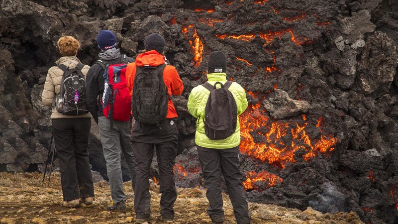 People watch as lava flows from an eruption of a volcano on the Reykjanes Peninsula in southwestern Iceland late on Monday, March 29, 2021. Iceland's latest volcano eruption is still attracting crowds of people hoping to get close to the gentle lava flows. (AP Photo/Marco Di Marco)