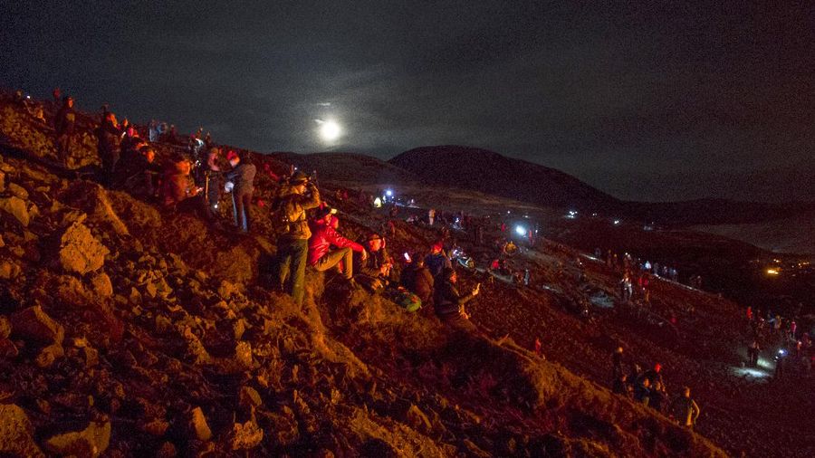 People watch as lava flows from an eruption of a volcano on the Reykjanes Peninsula in southwestern Iceland late on Monday, March 29, 2021. Iceland's latest volcano eruption is still attracting crowds of people hoping to get close to the gentle lava flows. (AP Photo/Marco Di Marco)