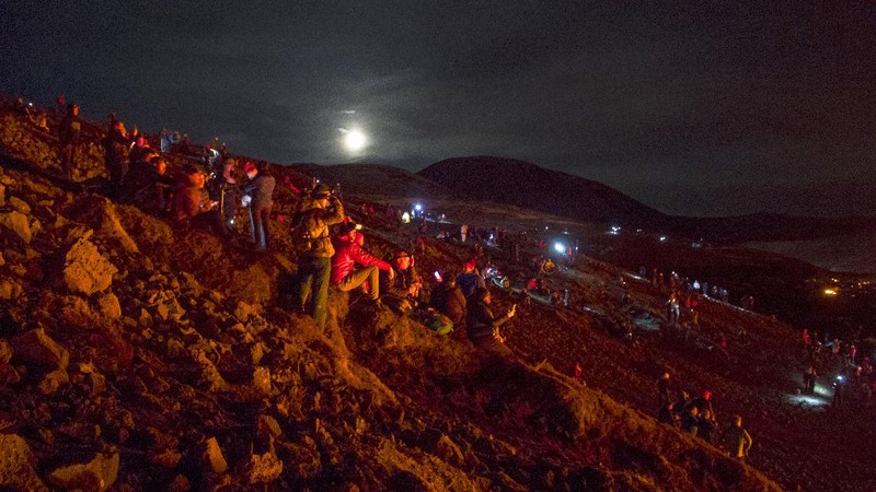 People watch as lava flows from an eruption of a volcano on the Reykjanes Peninsula in southwestern Iceland late on Monday, March 29, 2021. Iceland's latest volcano eruption is still attracting crowds of people hoping to get close to the gentle lava flows. (AP Photo/Marco Di Marco)