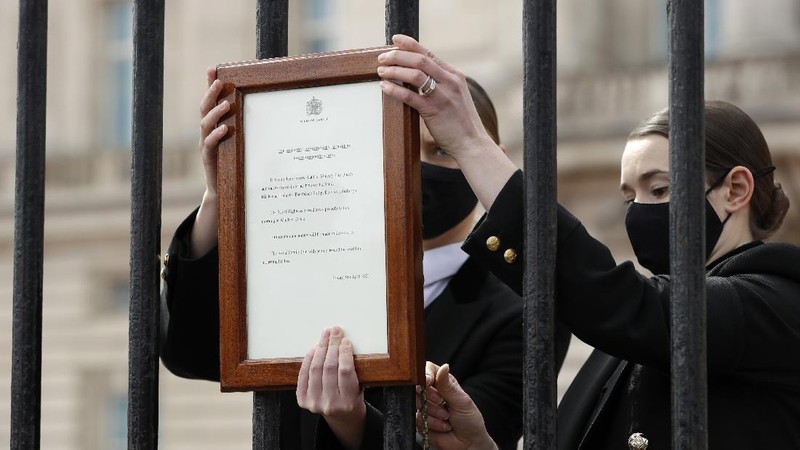 People view flowers left in front of the gate at Buckingham Palace in London, after the announcement of the death of Britain's Prince Philip, Friday, April 9, 2021. Buckingham Palace officials say Prince Philip, the husband of Queen Elizabeth II, has died. He was 99. Philip spent a month in hospital earlier this year before being released on March 16 to return to Windsor Castle. (AP Photo/Matt Dunham)