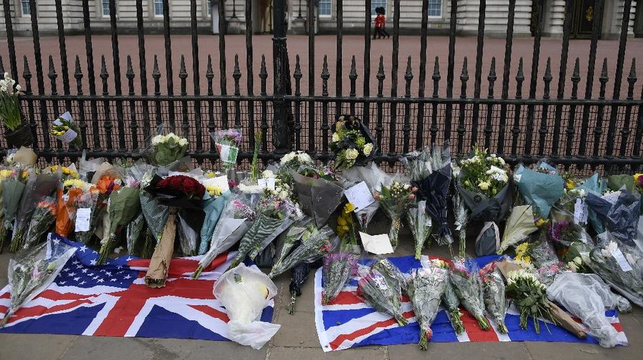 People view flowers left in front of the gate at Buckingham Palace in London, after the announcement of the death of Britain's Prince Philip, Friday, April 9, 2021. Buckingham Palace officials say Prince Philip, the husband of Queen Elizabeth II, has died. He was 99. Philip spent a month in hospital earlier this year before being released on March 16 to return to Windsor Castle. (AP Photo/Matt Dunham)