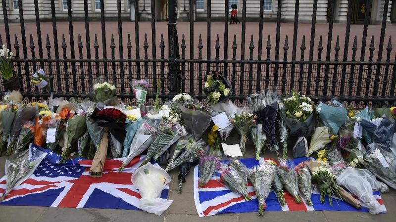 People view flowers left in front of the gate at Buckingham Palace in London, after the announcement of the death of Britain's Prince Philip, Friday, April 9, 2021. Buckingham Palace officials say Prince Philip, the husband of Queen Elizabeth II, has died. He was 99. Philip spent a month in hospital earlier this year before being released on March 16 to return to Windsor Castle. (AP Photo/Matt Dunham)