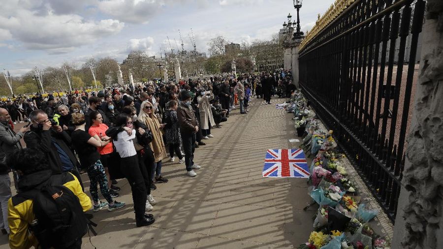 People view flowers left in front of the gate at Buckingham Palace in London, after the announcement of the death of Britain's Prince Philip, Friday, April 9, 2021. Buckingham Palace officials say Prince Philip, the husband of Queen Elizabeth II, has died. He was 99. Philip spent a month in hospital earlier this year before being released on March 16 to return to Windsor Castle. (AP Photo/Matt Dunham)