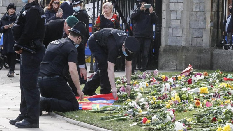 People view flowers left in front of the gate at Buckingham Palace in London, after the announcement of the death of Britain's Prince Philip, Friday, April 9, 2021. Buckingham Palace officials say Prince Philip, the husband of Queen Elizabeth II, has died. He was 99. Philip spent a month in hospital earlier this year before being released on March 16 to return to Windsor Castle. (AP Photo/Matt Dunham)
