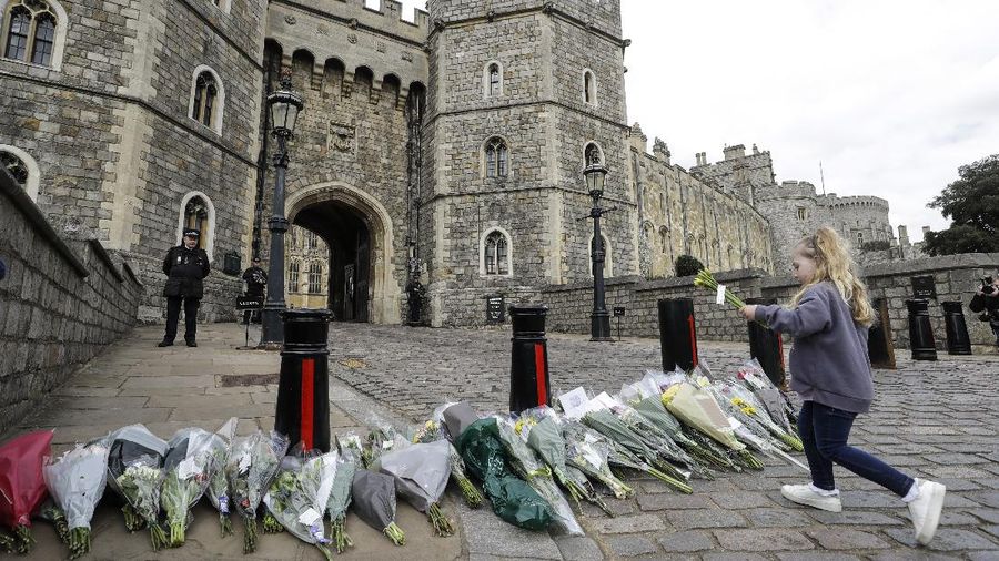 People view flowers left in front of the gate at Buckingham Palace in London, after the announcement of the death of Britain's Prince Philip, Friday, April 9, 2021. Buckingham Palace officials say Prince Philip, the husband of Queen Elizabeth II, has died. He was 99. Philip spent a month in hospital earlier this year before being released on March 16 to return to Windsor Castle. (AP Photo/Matt Dunham)