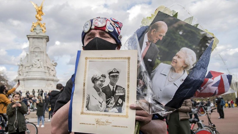 People view flowers left in front of the gate at Buckingham Palace in London, after the announcement of the death of Britain's Prince Philip, Friday, April 9, 2021. Buckingham Palace officials say Prince Philip, the husband of Queen Elizabeth II, has died. He was 99. Philip spent a month in hospital earlier this year before being released on March 16 to return to Windsor Castle. (AP Photo/Matt Dunham)