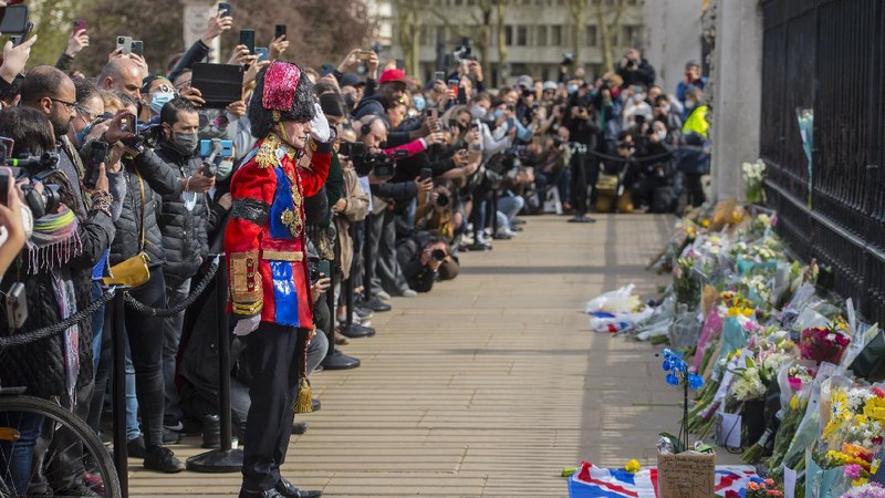 People view flowers left in front of the gate at Buckingham Palace in London, after the announcement of the death of Britain's Prince Philip, Friday, April 9, 2021. Buckingham Palace officials say Prince Philip, the husband of Queen Elizabeth II, has died. He was 99. Philip spent a month in hospital earlier this year before being released on March 16 to return to Windsor Castle. (AP Photo/Matt Dunham)