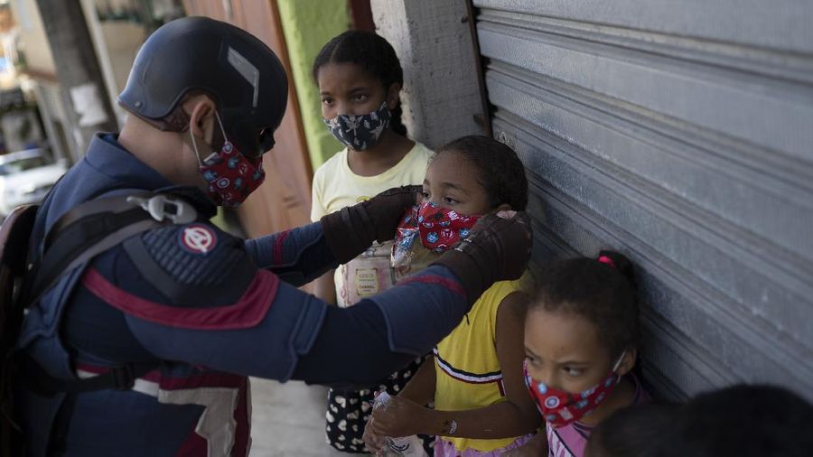 Military police officer Everaldo Pinto, dressed as superhero Captain America, places protective masks over children's mouths amid the COVID-19 pandemic in Petropolis, Rio de Janeiro state, Brazil, Thursday, April 15, 2021. Pinto advises children on the need to protect themselves against the COVID-19, distributing kits equipped with cleaning products and protective face masks to prevent the spread of the new coronavirus. (AP Photo/Silvia Izquierdo)