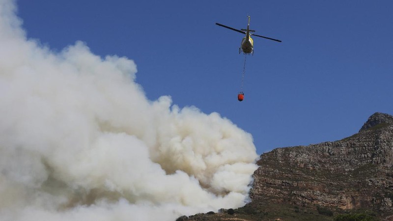 A helicopter drops water over a fire at Rhodes Memorial on Table Mountain, Cape Town, South Africa, Sunday, April 18, 2021. A wildfire raging on the slopes of the mountain forced the evacuation of students from the University of Cape Town. (AP Photo/Nardus Engelbrecht)