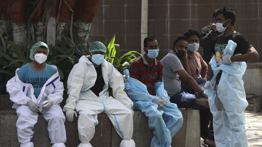 Health workers rest in between cremating COVID-19 victims in New Delhi, India, Monday, April 19, 2021. India has been overwhelmed by hundreds of thousands of new coronavirus cases daily, bringing pain, fear and agony to many lives as lockdowns have been placed in Delhi and other cities around the country. (AP Photo/Manish Swarup)