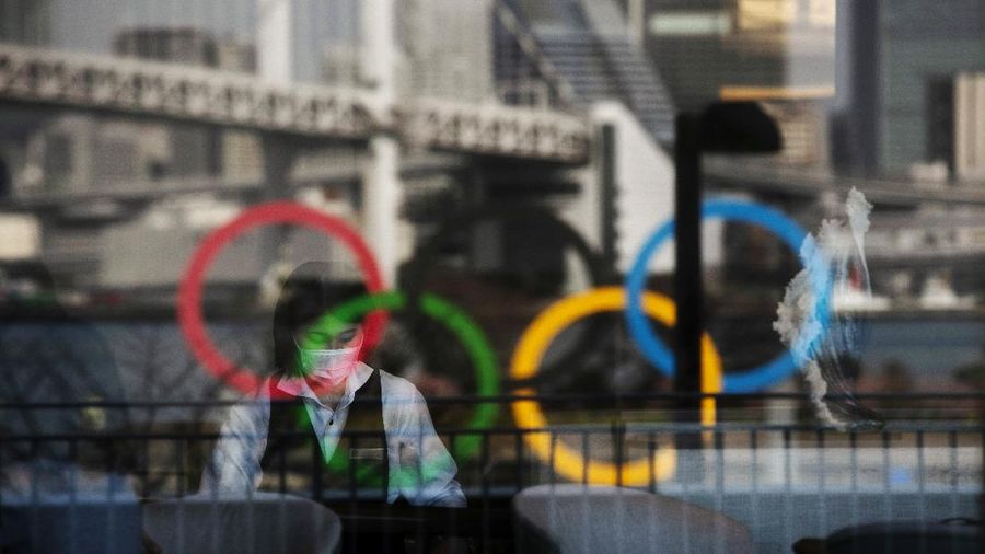 FILE - In this Feb. 24, 2020, photo, the Olympics rings are reflected on the window of a hotel restaurant as a server with a mask sets up a table, in the Odaiba section of Tokyo. The vaccine rollout in Japan has been very slow with less than 1% vaccinated. This of course is spilling over to concerns about the postponed Tokyo Olympics that open in just over three months.(AP Photo/Jae C. Hong, File)