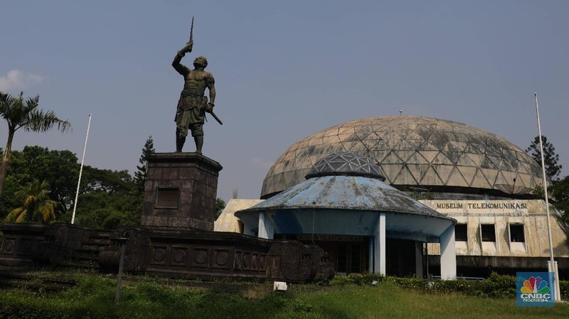 Suasana kondisi museum telekomunikasi yang sudah tidak terpakai di Kawasan TMII, Jakarta, Senin (26/4). Setelah tidak beroperasi akibat pandemi, pengelola membuka kembali TMII dengan menerapkan protokol kesehatan pencegahan COVID-19 dan pembatasan pengunjung.  Pantauan CNBC Indonesia beberapa wahana dan anjungan tidak terawat. TMII yang merupakan aset penting untuk mengajarkan kepada generasi penerus mengenai budaya, seni, dan beragamnya Indonesia. Seperti halnya di museum minyak gas bumi banyak rumput-rumput liar yang tumbuh disekitar bangunan. Mampir ke Anjungan Riau, menyaksikan pemandangan yang kurang lebih sama. Tak ada antrean di loket. Hanya ada beberapa warga yang tertidur di bawah rumah. Kebijakan Presiden Jokowi mengambil alih kembali aset-aset negara dari anak-anak Soeharto menjadi sorotan belakangan. Setelah pimpinan negara yang lalu tak melakukan langkah serupa Jokowi. Pengambil alihan aset taman mini sudah dituangkan dalam Peraturan Presiden (Perpres) Nomor 19 Tahun 2021 tentang mengambil alih pengolahan TMII yang diterbitkan Jokowi.  (CNBC Indonesia/ Muhammad Sabki)