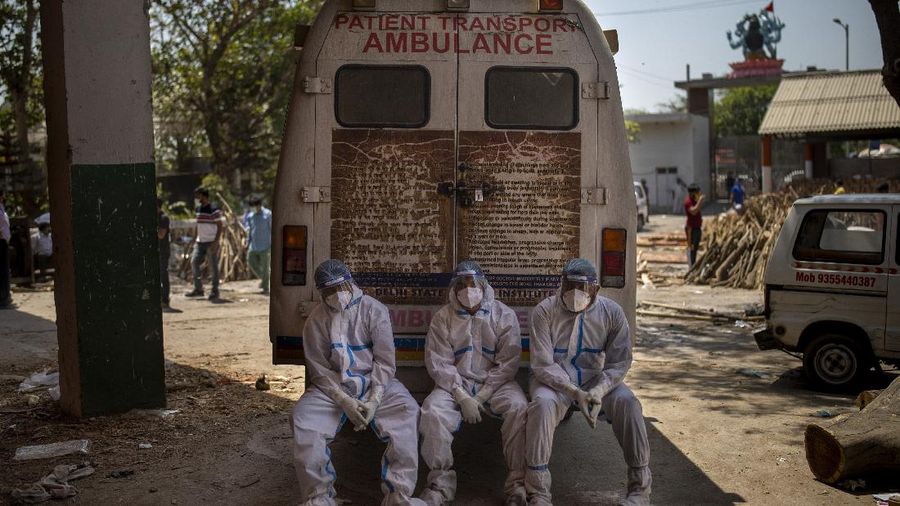 Exhausted workers, who bring dead bodies for cremation, sit on the rear step of an ambulance inside a crematorium, in New Delhi, India, Saturday, April 24, 2021. As India suffers a bigger, more infectious second wave with a caseload of more than 300,000 new cases a day, the country’s healthcare workers are bearing the brunt of the disaster. (AP Photo/Altaf Qadri)