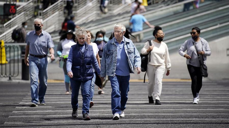 Masked and unmasked pedestrians walk across Las Vegas Boulevard, Tuesday, April 27, 2021, in Las Vegas. The Centers for Disease Control and Prevention eased its guidelines Tuesday on the wearing of masks outdoors, saying fully vaccinated Americans don't need to cover their faces anymore unless they are in a big crowd of strangers. (AP Photo/John Locher)