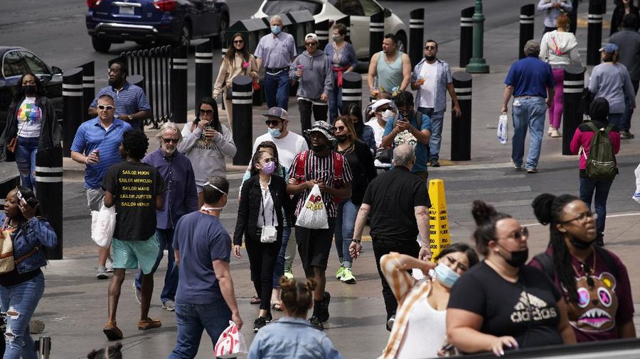 Masked and unmasked pedestrians walk along the Las Vegas Strip, Tuesday, April 27, 2021, in Las Vegas. The Centers for Disease Control and Prevention eased its guidelines Tuesday on the wearing of masks outdoors, saying fully vaccinated Americans don't need to cover their faces anymore unless they are in a big crowd of strangers.(AP Photo/John Locher)