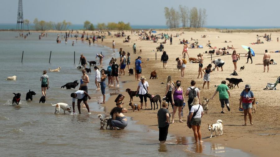 People gather with their dogs in Chicago's Montrose Dog Beach, Tuesday, April 27, 2021. The Centers for Disease Control and Prevention eased its guidelines Tuesday on the wearing of masks outdoors, saying fully vaccinated Americans don't need to cover their faces anymore unless they are in a big crowd of strangers. (AP Photo/Shafkat Anowar)