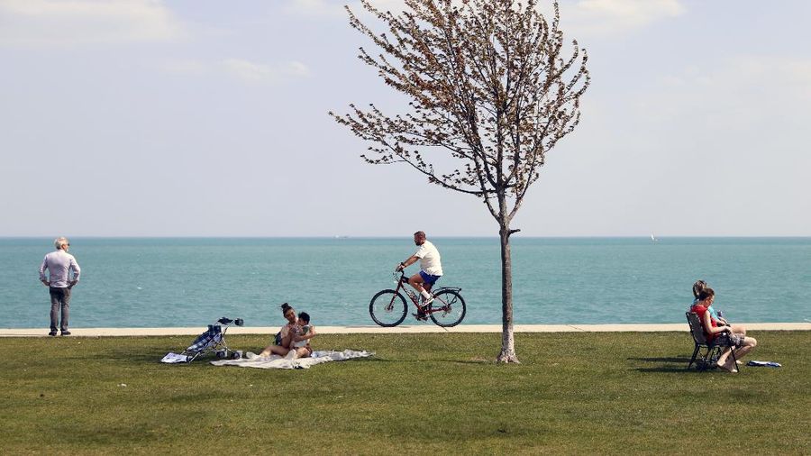 People spend time as they take advantage of warm spring weather along Lake Michigan on Tuesday, April 27, 2021, at Montrose Beach in Chicago. The Centers for Disease Control and Prevention eased its guidelines Tuesday on the wearing of masks outdoors, saying fully vaccinated Americans don't need to cover their faces anymore unless they are in a big crowd of strangers. (AP Photo/Shafkat Anowar)