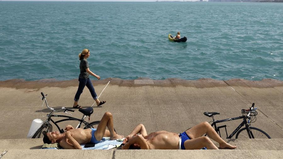 Chet Ski, left and Richard Paul sunbath as others pass along Lake Michigan on Tuesday, April 27, 2021 in Montrose Beach, Chicago. The Centers for Disease Control and Prevention eased its guidelines Tuesday on the wearing of masks outdoors, saying fully vaccinated Americans don't need to cover their faces anymore unless they are in a big crowd of strangers. (AP Photo/Shafkat Anowar)