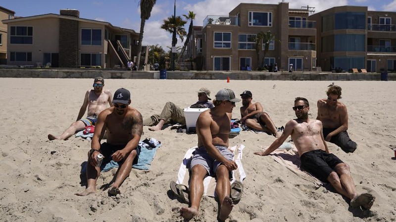 A group of men in town for a bachelor's party sit on the beach Tuesday, April 27, 2021, in San Diego. Many in the group had already been vaccinated. U.S. health officials say fully vaccinated Americans don't need to wear masks outdoors anymore unless they are in a big crowd of strangers. And unvaccinated people can drop face coverings in some cases, too. (AP Photo/Gregory Bull)