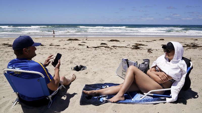 A group of men in town for a bachelor's party sit on the beach Tuesday, April 27, 2021, in San Diego. Many in the group had already been vaccinated. U.S. health officials say fully vaccinated Americans don't need to wear masks outdoors anymore unless they are in a big crowd of strangers. And unvaccinated people can drop face coverings in some cases, too. (AP Photo/Gregory Bull)