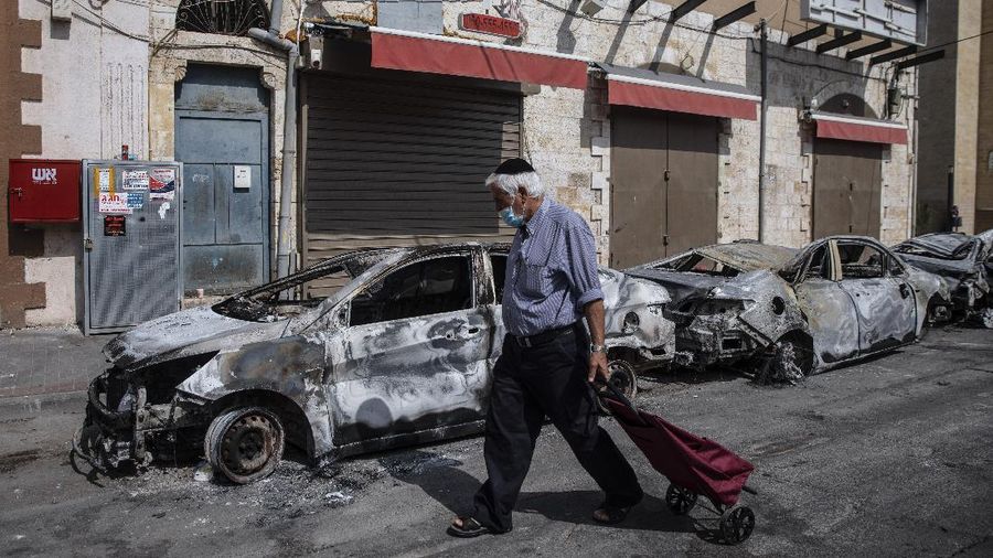 A man passes by cars torched after a night of violence between Israeli Arab protesters and Israeli police in the mixed Arab-Jewish town of Lod, central Israel, Tuesday, May 11, 2021. (AP Photo/Heidi Levine)