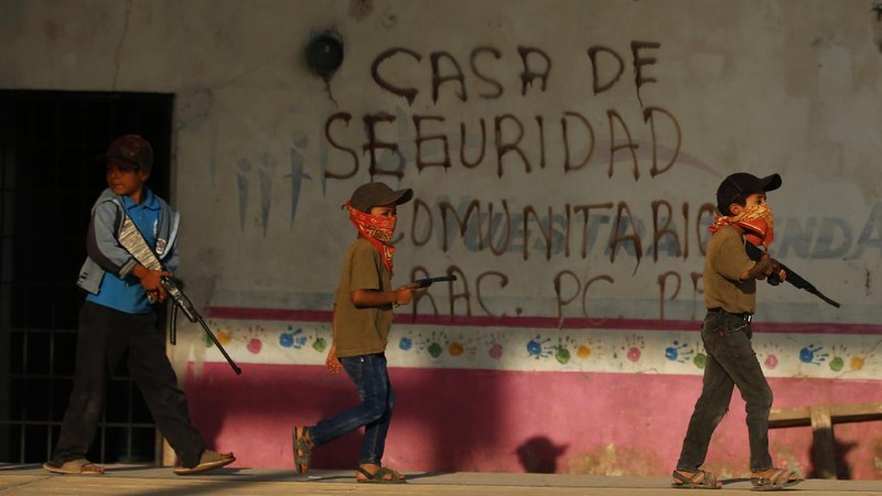 Children train with fake weapons during a display for the media designed to to attract the federal government's attention to the dangers of organized crime their town negotiates daily in Ayahualtempa, Guerrero state, Mexico, Wednesday, April 28, 2021. This long-abandoned and violent region is one of Mexico's poorest and also a key corridor for drug production and transit, especially heroin from opium poppies. (AP Photo/Marco Ugarte)