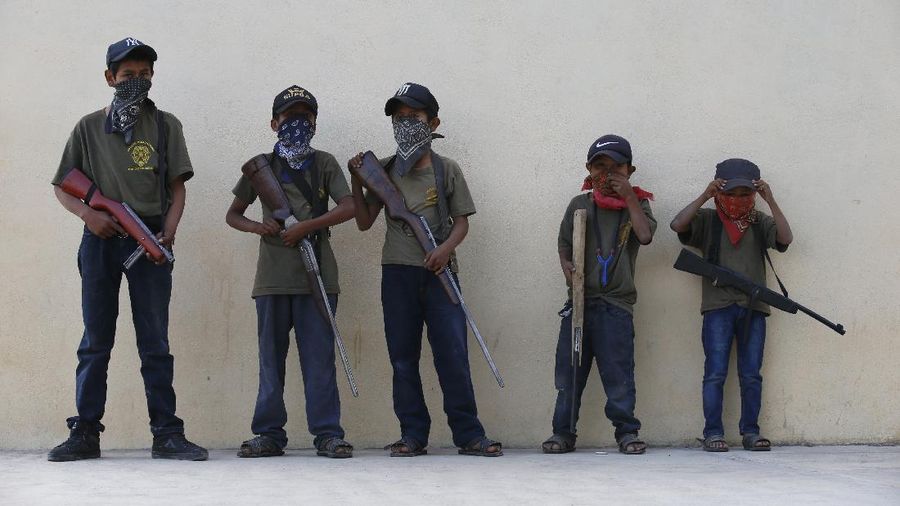 Children train with fake weapons during a display for the media designed to to attract the federal government's attention to the dangers of organized crime their town negotiates daily in Ayahualtempa, Guerrero state, Mexico, Wednesday, April 28, 2021. This long-abandoned and violent region is one of Mexico's poorest and also a key corridor for drug production and transit, especially heroin from opium poppies. (AP Photo/Marco Ugarte)
