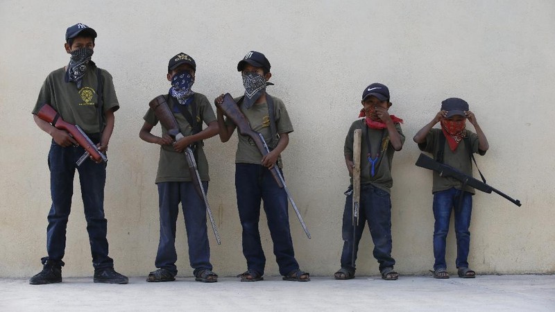 Children train with fake weapons during a display for the media designed to to attract the federal government's attention to the dangers of organized crime their town negotiates daily in Ayahualtempa, Guerrero state, Mexico, Wednesday, April 28, 2021. This long-abandoned and violent region is one of Mexico's poorest and also a key corridor for drug production and transit, especially heroin from opium poppies. (AP Photo/Marco Ugarte)