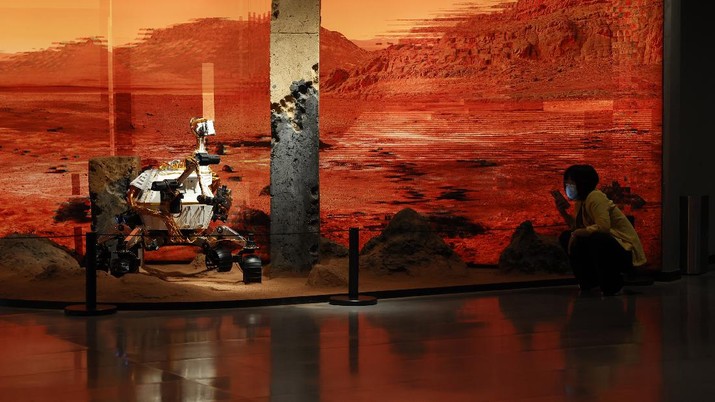 China Space Mars Mission A woman wearing a mask talks on her phone near an exhibition depicting a rover in Mars in Beijing on Friday, May 14, 2021. China says its Mars probe and accompanying rover are to land on the red planet sometime between early Saturday morning and Wednesday Beijing time. (AP Photo/Ng Han Guan)