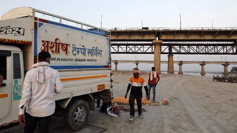 Policemen stand next to the bodies buried in shallow graves on the banks of Ganges river in Prayagraj, India, Saturday, May 15, 2021. Police are reaching out to villagers in northern India to investigate the recovery of bodies buried in shallow sand graves or washing up on the Ganges River banks, prompting speculation on social media that they were the remains of COVID-19 victims. (AP Photo/Rajesh Kumar Singh)