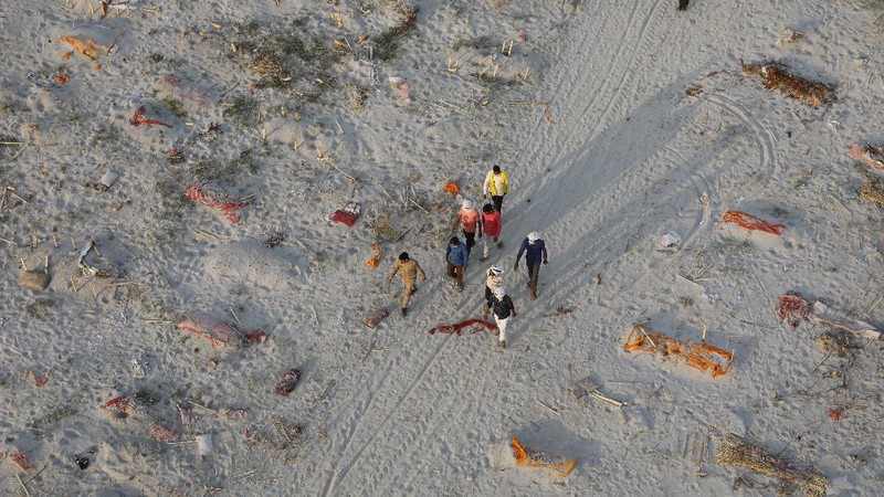 Policemen stand next to the bodies buried in shallow graves on the banks of Ganges river in Prayagraj, India, Saturday, May 15, 2021. Police are reaching out to villagers in northern India to investigate the recovery of bodies buried in shallow sand graves or washing up on the Ganges River banks, prompting speculation on social media that they were the remains of COVID-19 victims. (AP Photo/Rajesh Kumar Singh)