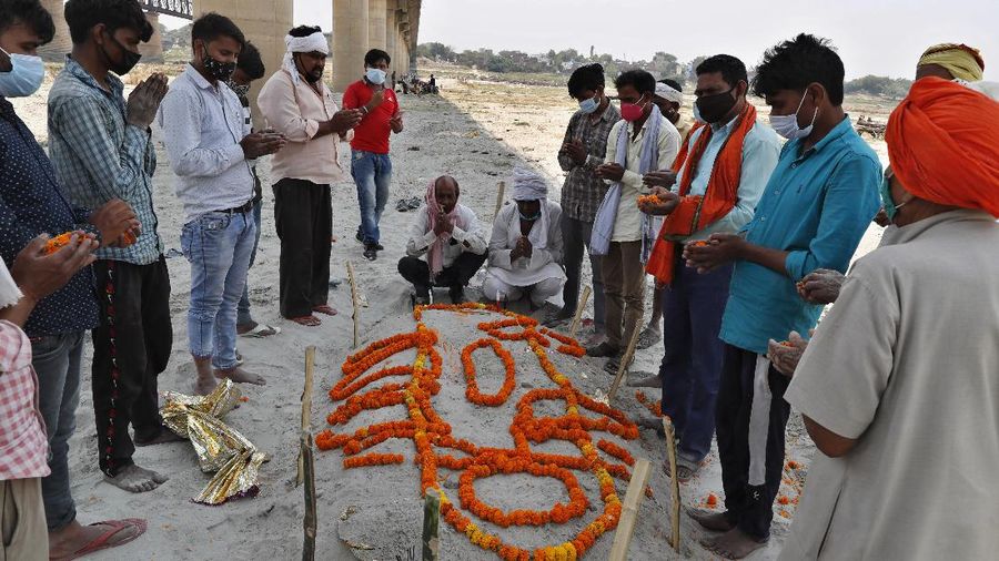 Policemen stand next to the bodies buried in shallow graves on the banks of Ganges river in Prayagraj, India, Saturday, May 15, 2021. Police are reaching out to villagers in northern India to investigate the recovery of bodies buried in shallow sand graves or washing up on the Ganges River banks, prompting speculation on social media that they were the remains of COVID-19 victims. (AP Photo/Rajesh Kumar Singh)