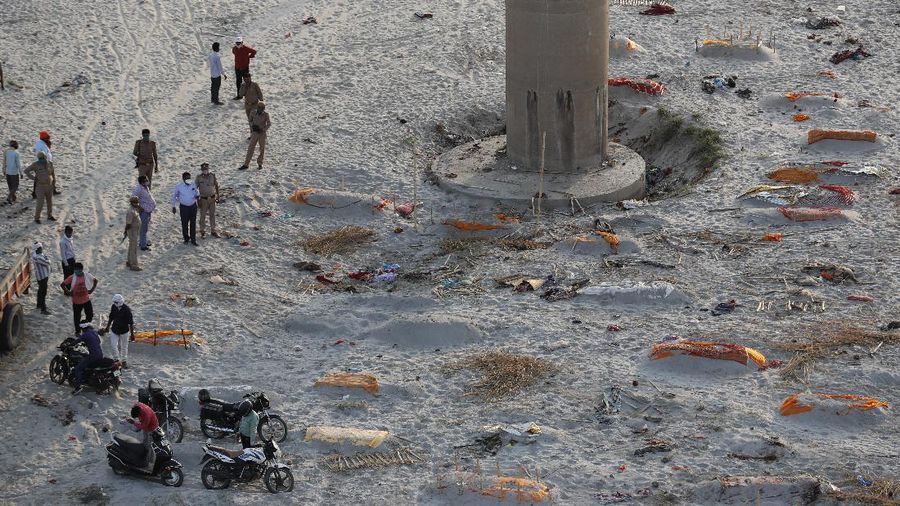 Policemen stand next to the bodies buried in shallow graves on the banks of Ganges river in Prayagraj, India, Saturday, May 15, 2021. Police are reaching out to villagers in northern India to investigate the recovery of bodies buried in shallow sand graves or washing up on the Ganges River banks, prompting speculation on social media that they were the remains of COVID-19 victims. (AP Photo/Rajesh Kumar Singh)