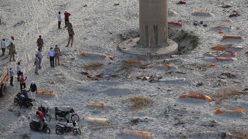Policemen stand next to the bodies buried in shallow graves on the banks of Ganges river in Prayagraj, India, Saturday, May 15, 2021. Police are reaching out to villagers in northern India to investigate the recovery of bodies buried in shallow sand graves or washing up on the Ganges River banks, prompting speculation on social media that they were the remains of COVID-19 victims. (AP Photo/Rajesh Kumar Singh)