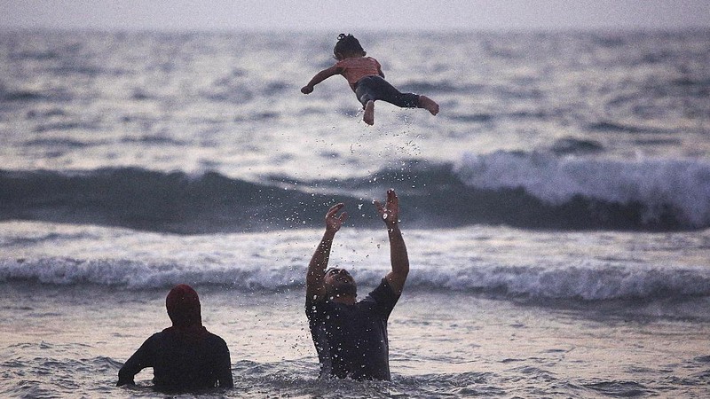 A Palestinians man plays with his child as the family enjoys a day at the beach of the Mediterranean sea in Gaza City, Friday, Sept. 18, 2020. (AP Photo/Hatem Moussa)