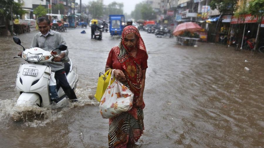 A motorist and a woman wade through a waterlogged street after heavy rains in Ahmedabad, India, Tuesday, May 18, 2021. Cyclone Tauktae, the most powerful storm to hit the region in more than two decades, packed sustained winds of up to 210 kilometers (130 miles) per hour when it came ashore in Gujarat state late Monday. (AP Photo/Ajit Solanki)