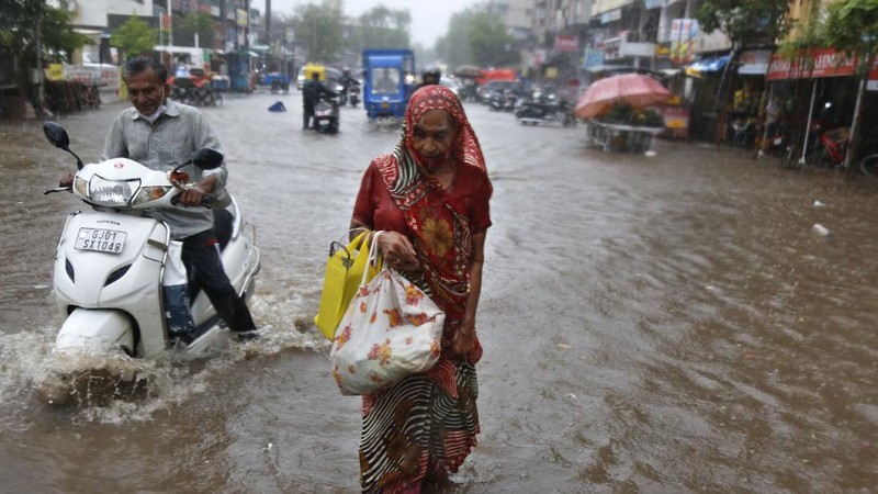 A motorist and a woman wade through a waterlogged street after heavy rains in Ahmedabad, India, Tuesday, May 18, 2021. Cyclone Tauktae, the most powerful storm to hit the region in more than two decades, packed sustained winds of up to 210 kilometers (130 miles) per hour when it came ashore in Gujarat state late Monday. (AP Photo/Ajit Solanki)