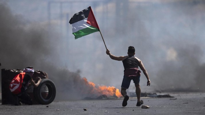 Warga Palestina Bentrok di Tepi Barat Seorang pengunjuk rasa mengibarkan bendera Palestina selama bentrokan dengan pasukan Israel di pos pemeriksaan Hawara, selatan kota Nablus, Tepi Barat, Jumat, 14 Mei 2021. Pejabat kesehatan mengatakan beberapa warga Palestina tewas oleh tembakan tentara Israel, pada protes yang terjadi di beberapa lokasi di Tepi Barat hari Jumat. (AP / Majdi Mohammed)