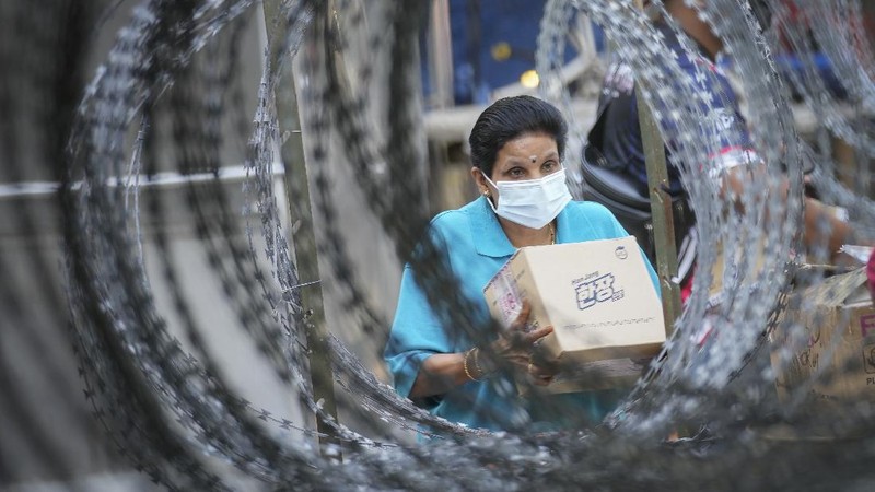 A resident wearing a face mask collects her package behind barbed wire outside the Pangsapuri Permai housing which is placed under the enhanced movement control order (EMCO) due to the drastic increase in the number of Covid-19 cases recorded over the past 10 days in Cheras, outside Kuala Lumpur, Malaysia, Friday, May 28, 2021. Malaysia's latest coronavirus surge has been taking a turn for the worse as surging numbers and deaths have caused alarm among health officials, while cemeteries in the capital are dealing with an increasing number of deaths. (AP Photo/Vincent Thian)