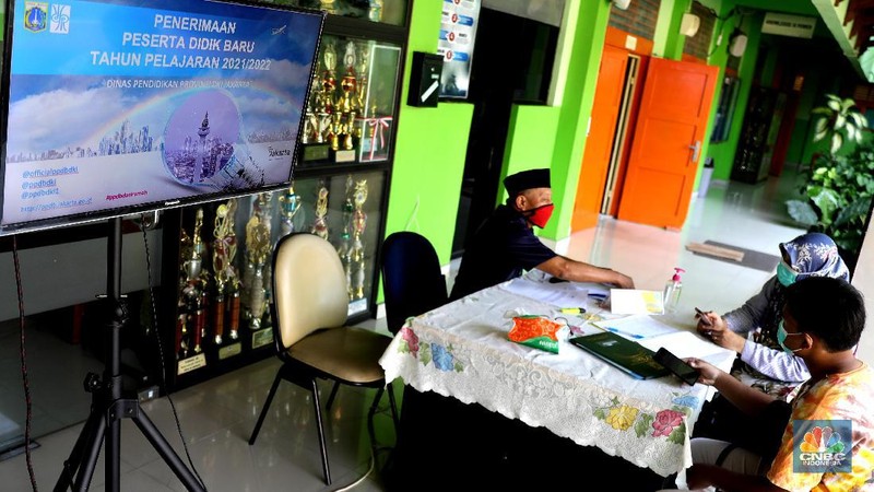 Orang tua murid mencari informasi pengajuan akun untuk mengikuti proses penerimaan Peserta Didik Baru (PPDB) Tahun Pelajaran 2021/2022 di Sekolah SMA Negeri 87 Jakarta, Senin (7/6). Proses penerimaan Peserta Didik Baru (PPDB) Tahun Pelajaran 2021/2022 di DKI Jakarta yang mulai dibuka sejak hari ini, Senin (7/6). Pada tahun ini, ada empat jalur pendaftaran yang dibuka meliputi jalur prestasi, afirmasi, zonasi, perpindahan tugas orang tua dan anak guru. Pada hari ini 7 Juni hingga 9 Juni 2021 PPDB dibuka khusus untuk jalur prestasi. Persyaratan PPDB Jakarta 2021 adalah ketentuan yang mewajibkan bahwa sekolah-sekolah negeri atau milik pemerintah yang ada di wilayah DKI Jakarta, hanya boleh menerima siswa yang terdaftar di Kartu Keluarga (KK) yang diterbitkan oleh Dinas Catatan Sipil dan Kependudukan Provinsi DKI Jakarta. Aturan ini PPDB DKI Jakarta 2021 juga telah diundangkan pada tanggal yang sama, dan dicatatkan dalam Berita Daerah Provinsi DKI Jakarta Tahun 2021 nomor 55005.
Pada pasal 1 ayat (11) Pergub No 32 Tahun 2021 tersebut meyebutkan, 