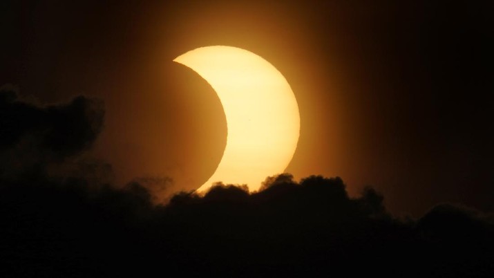 Gerhana matahari cincin sebagian muncul dari balik awan saat terbit di atas Manhattan di New York, Kamis (10/6/2021). (AP Photo/Seth Wenig) A partially eclipsed sun peaks out from behind a cloud as it rises over lower Manhattan in New York, Thursday, June 10, 2021. (AP Photo/Seth Wenig)
