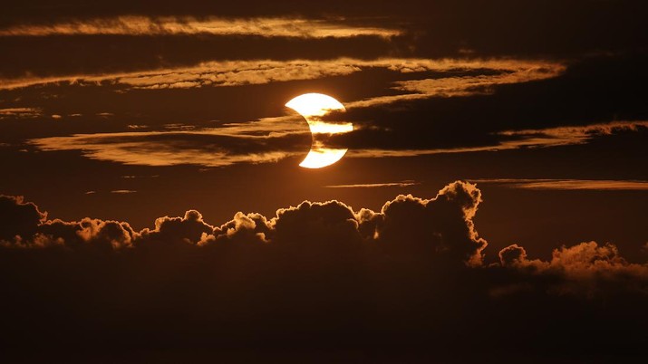 A partial solar eclipse rises behind clouds, Thursday, June 10, 2021, in Arbutus, Md. (AP Photo/Julio Cortez)