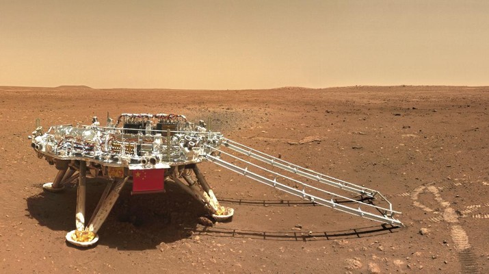 Platform pendaratan dengan bendera nasional China di Mars terlihat dari rover Zhurong In this image released by the China National Space Administration (CNSA) on Friday, June 11, 2021, the landing platform with a Chinese national flag and outlines of the mascots for the 2022 Beijing Winter Olympics and Paralympics on Mars is seen from the rover Zhurong. China on Friday released a series of photos taken by its Zhurong rover on the surface of Mars, including one of the rover itself taken by a remote camera. (CNSA via AP)