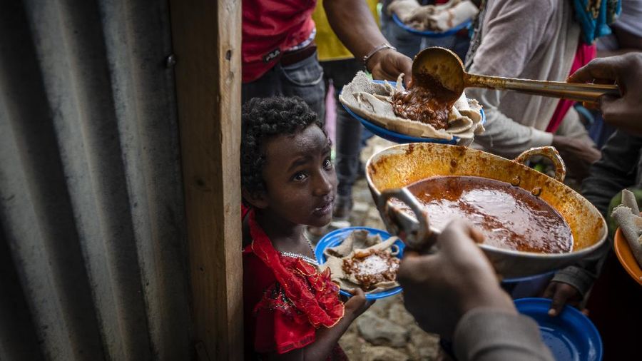Elena, 7, center, lines up with other displaced Tigrayans to receive food donated by local residents at a reception center for the internally displaced in Mekele, in the Tigray region of northern Ethiopia, on Sunday, May 9, 2021. The 15 kilograms of wheat, half a kilogram of peas and some cooking oil per person, to last a month — was earmarked only for the most vulnerable. That included pregnant mothers and elderly people. (AP Photo/Ben Curtis)