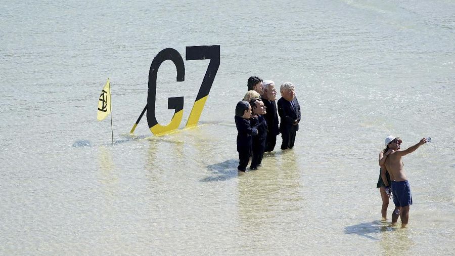 Para pengunjuk rasa mengenakan topeng yang menggambarkan para pemimpin G7 di pantai di Cornwall, Inggris. (AP/Jon Super)