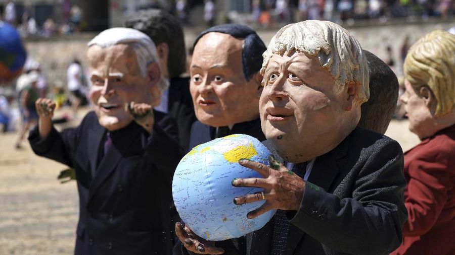 Para pengunjuk rasa mengenakan topeng yang menggambarkan para pemimpin G7 di pantai di Cornwall, Inggris. (AP/Jon Super)